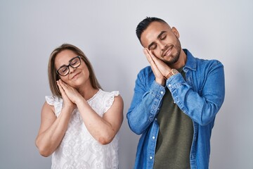 Hispanic mother and son standing together sleeping tired dreaming and posing with hands together while smiling with closed eyes.