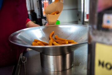 Freshly fried churros lie in a pan before being served in a paper bag