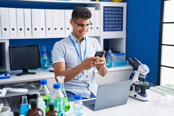 Young hispanic man scientist using laptop and smartphone at laboratory