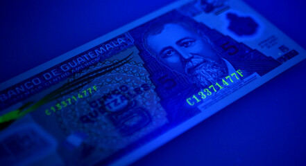 Guatemalan banknotes under UV light. Checking for counterfeit money. Close-up Guatemala quetzales....