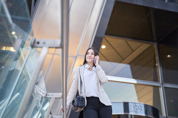 Smiling business woman talking on cell phone outside office building.