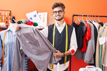Young hispanic man tailor smiling confident holding shirt at atelier