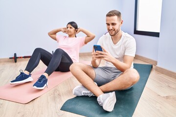 Fototapeta na wymiar Man and woman couple smiling confident training abs exercise using smartphone at sport center