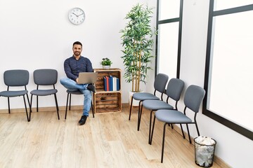 Young hispanic man using laptop sitting on chair at waiting room