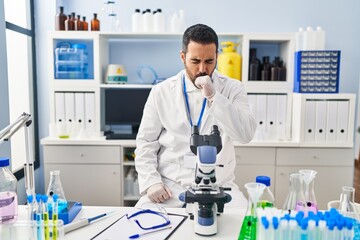 Young hispanic man with beard working at scientist laboratory feeling unwell and coughing as symptom for cold or bronchitis. health care concept.