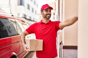 Young hispanic man courier holding package press doorbell at street