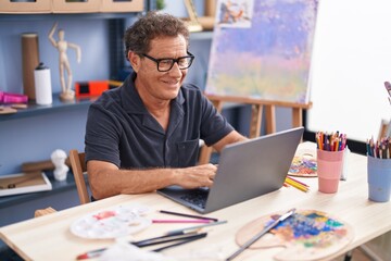 Middle age man artist smiling confident using laptop at art studio