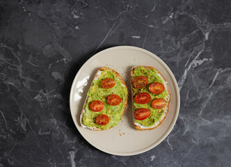 Toast with avocado and cherry tomatoes on a white plate. Top view.