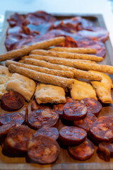 Wooden plate with sliced Spanish tapas, choriso sausage, lomo iberico en bread sticks