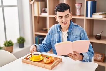 Fototapeta premium Young non binary man reading book having breakfast at home