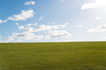 Obraz premium Rasen (Deich) mit blauem Himmel und vereinzelt Wolken