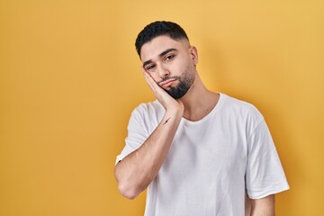 Young handsome man wearing casual t shirt over yellow background thinking looking tired and bored with depression problems with crossed arms.