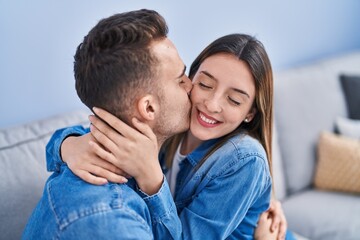 Fototapeta premium Man and woman couple sitting on sofa hugging each other and kissing at home