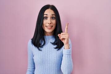 Hispanic woman standing over pink background pointing finger up with successful idea. exited and happy. number one.