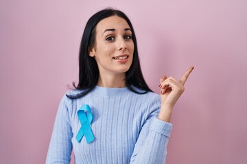 Hispanic woman wearing blue ribbon smiling happy pointing with hand and finger to the side