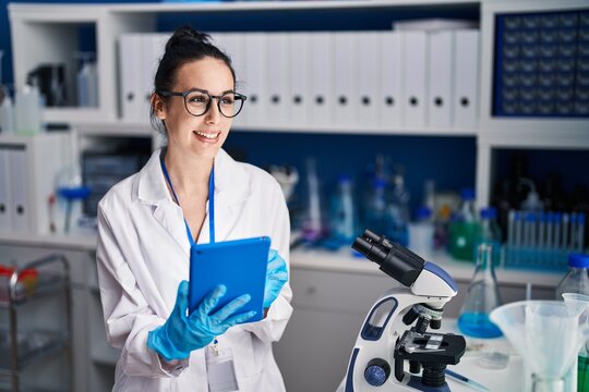 Young caucasian woman scientist smiling confident using touchpad at laboratory