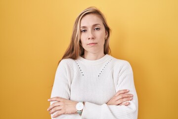 Fototapeta premium Young caucasian woman wearing white sweater over yellow background skeptic and nervous, disapproving expression on face with crossed arms. negative person.