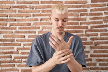 Young caucasian man standing over bricks wall suffering pain on hands and fingers, arthritis inflammation