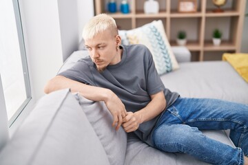 Young caucasian man sitting on sofa with serious expression at home