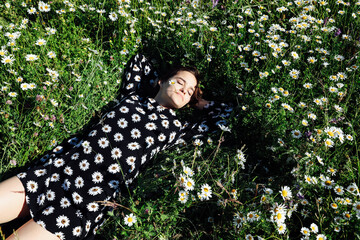 a woman in a dress with daisies lies in a field of flowers