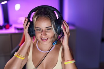 Young blonde woman streamer smiling confident sitting on table at gaming room