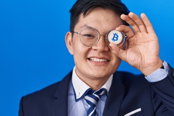 Young asian man holding virtual currency bitcoin covering eye smiling with a happy and cool smile on face. showing teeth.