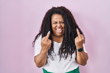 Plus size hispanic woman standing over pink background showing middle finger doing fuck you bad...