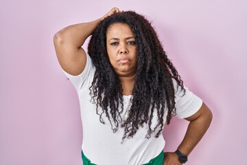 Plus size hispanic woman standing over pink background confuse and wondering about question. uncertain with doubt, thinking with hand on head. pensive concept.