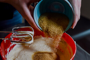 hands adding brown sugar to white cheese and eggs being whipped together to make cheesecake cream