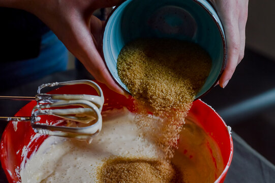 hands adding brown sugar to white cheese and eggs being whipped together to make cheesecake cream