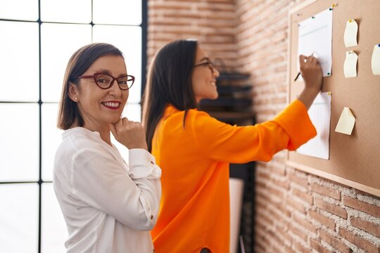 Two women business workers writing on cork board at office