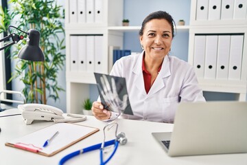 Middle age hispanic woman wearing doctor uniform holding xray at clinic