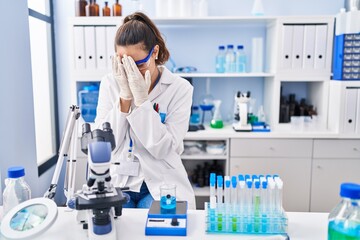 Fototapeta premium Young hispanic woman working at scientist laboratory with sad expression covering face with hands while crying. depression concept.