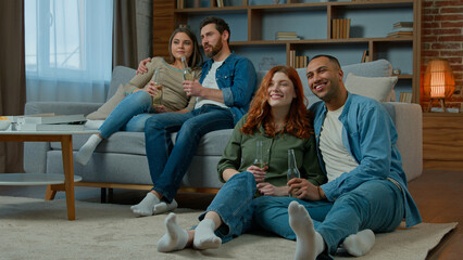 Two ethnic couple diverse men women watch television romantic tv film at home family rest on sofa and floor multiracial friends watching comedy movie comfortable leisure in apartment with bottled beer
