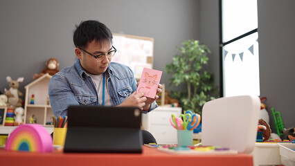 Young chinese man preschool teacher having online vocabulary lesson at kindergarten