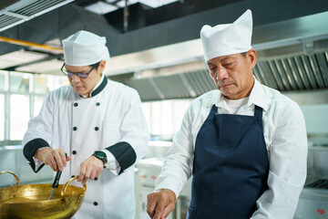 Happy Asian professional chef cooking in kitchen in Asian restaurant. Males professional chef cooking in Chinese kitchen.