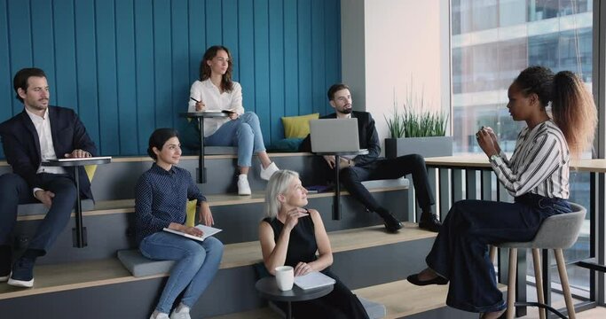 Multiracial team listen African woman, business trainer during training in co-working space. Corporate seminar, new knowledge, develop skills, university educational workshop event in modern auditory
