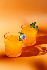 orange cocktail with mint and violet on orange background