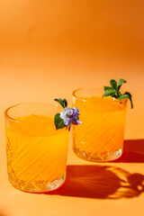 orange cocktail with mint and violet on orange background