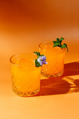 orange cocktail with mint and violet on orange background