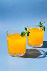 orange cocktail with mint and orange chips on a blue background