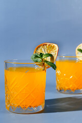 orange cocktail with mint and orange chips on a blue background