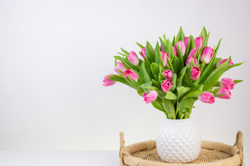 white vase with tulips and handmade wicker rattan tray on white background. Space for text on the left