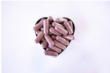 Pink capsules with supplements on a white background in the shape of a heart. Tablets and medications