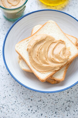 White plate with bread slices and peanut butter for making sandwiches, vertical shot, middle close-up