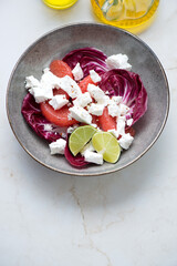 Salad with radicchio, grapefruit and goat cheese served in a grey bowl on a light-beige marble background, vertical shot