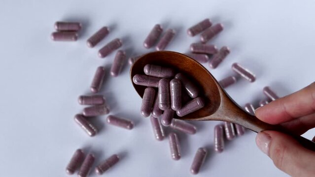 Pink capsules with supplements in a wooden spoon on a white background. Tablets and medicines. Vitamins, minerals, plant extracts and other useful substances. Tart Cherry