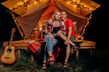 Happy lovely couple relaxing in glamping on evening near cozy bonfire. Luxury camping tent for outdoor recreation and recreation. Lifestyle concept - 577745102