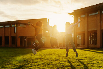 group of three young friends jumping together at the end of classes at the university or high...