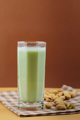 Plant-based natural pistachio milk on a beige background. Tall glass with pistachio milk on a linen napkin. Copy space